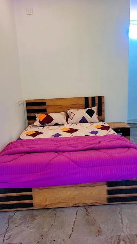 een slaapkamer met een houten bed met paarse lakens en kussens bij S N M ROOM in Malappuram