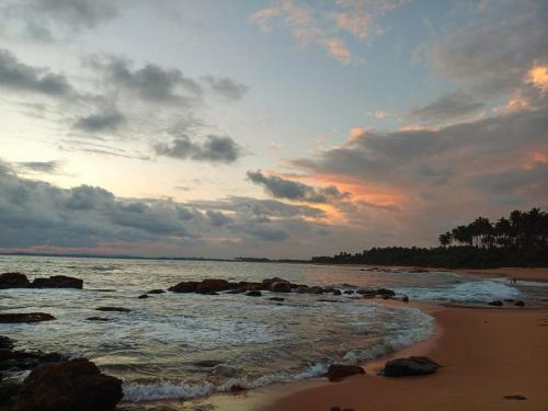a sunset on the beach with rocks in the water at Turtle Island Cabana in Tangalle