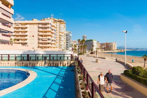 two people walking by a swimming pool next to a building at Apartamento Topacio 2 - PlusHolidays in Calpe