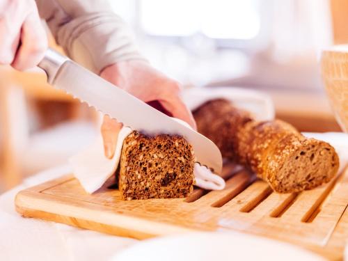 a person cutting a loaf of bread on a cutting board at Alpina Lech - Geborgen in den Bergen in Lech am Arlberg