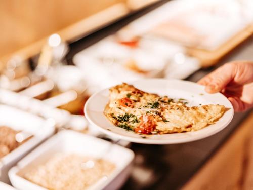 a person holding a plate with a slice of pizza at Alpina Lech - Geborgen in den Bergen in Lech am Arlberg