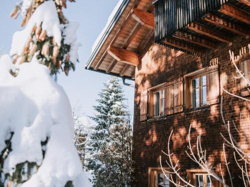 a building covered in snow next to a tree at Alpina Lech - Geborgen in den Bergen in Lech am Arlberg