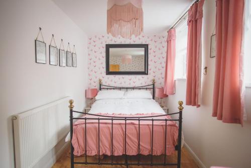 a small bedroom with a bed with pink walls at Hectors house in Ormesby Saint Michael