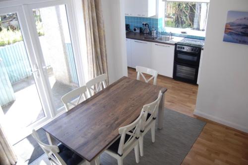 a kitchen with a wooden table and white chairs at Lovely cottage in Snowdonia, private hot tub, by mountains & award winning beach in Fairbourne