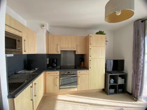 une cuisine avec des placards en bois et des comptoirs noirs dans l'établissement Appartement ⭐⭐ face à l'Étang de Thau, proche thermes, balcon et animaux bienvenus - FR-1-503-19, à Balaruc-les-Bains