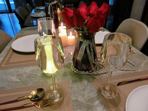 een tafel met twee wijnglazen en een vaas met rode rozen bij Mangrove Bay Riverside Hill Riverview B&Bl紅樹灣河畔山河景民宿l毗邻澳門l拱北l華發商都 in Zhuhai