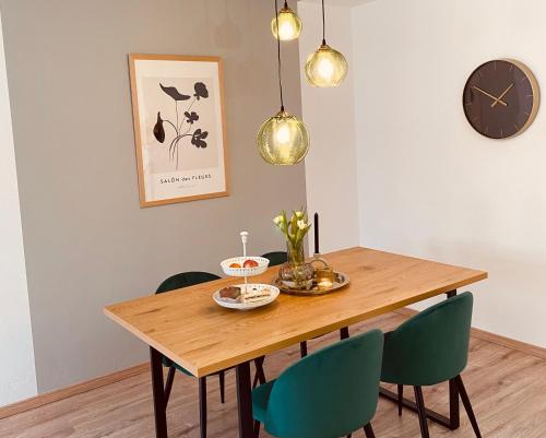 a dining room table with green chairs and a clock at Neu renovierte FeWo Moritz Nähe HUK in Coburg