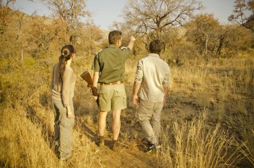 a group of three people walking through a field at Morokolo Safari Lodge Self-catering in Pilanesberg