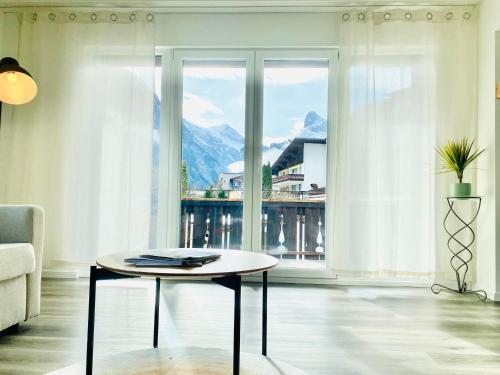 ein Wohnzimmer mit einem Tisch und einem großen Fenster in der Unterkunft Modern designed, luxury mountain view Apartment in Kandersteg