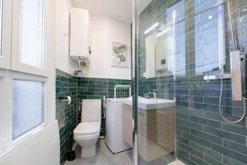 La salle de bains est pourvue de carrelage vert, de toilettes et d'un lavabo. dans l'établissement Studio Cosy à 15min de Paris et 5min du Métro, à La Courneuve
