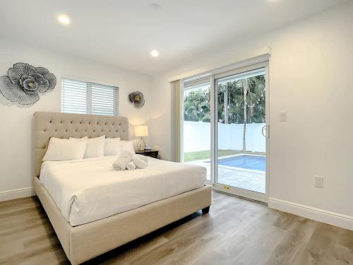 a white bedroom with a bed and a sliding glass door at Luxe Home - Heated Pool I 5 min to Beach I BBQ Grill in Fort Lauderdale