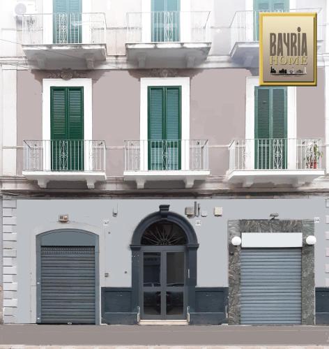 a white building with green shuttered windows and a sign at BAYRIA HOME in Bari