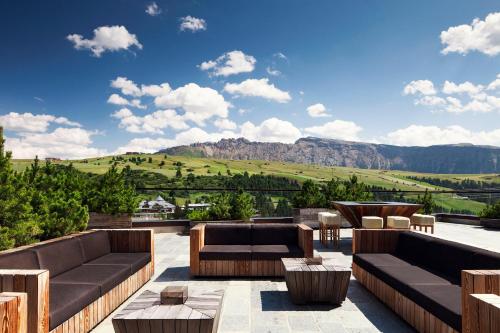 a patio with couches and tables and a view of mountains at COMO Alpina Dolomites in Alpe di Siusi