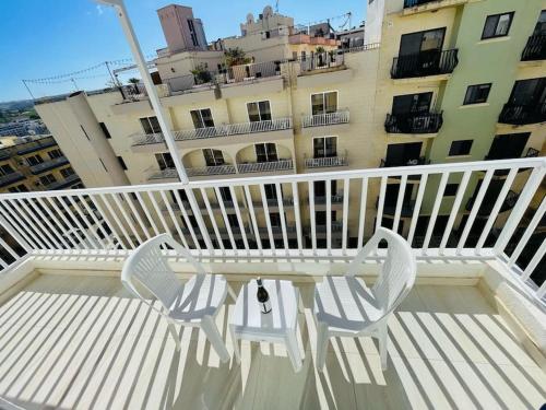 - deux chaises blanches assises sur le balcon d'un bâtiment dans l'établissement Coral Cove Comfort Room 1, à San Pawl il-Baħar