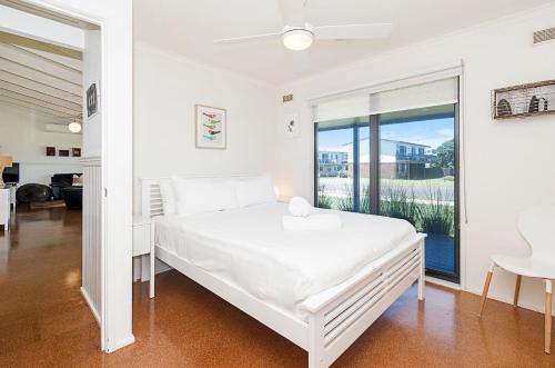 a white bedroom with a bed and a large window at Ocean Spray Retreat in Port Fairy
