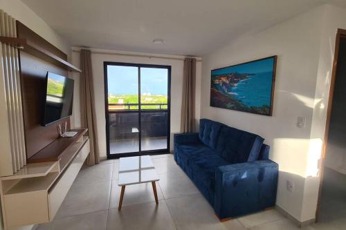 ein Wohnzimmer mit einem blauen Sofa und einem großen Fenster in der Unterkunft Aconchego em Carapibus 2-Cobertura Nascente Sul in Conde
