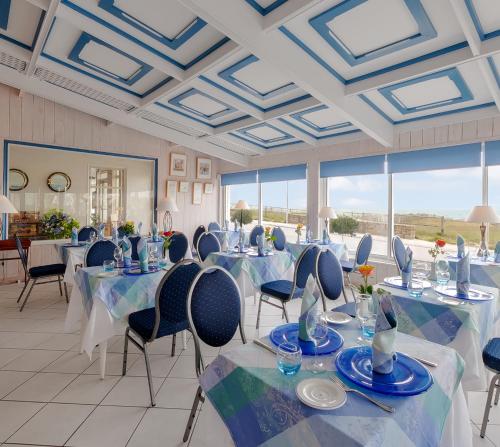 une salle de banquet avec des tables et des chaises bleues ainsi que des fenêtres dans l'établissement Hotel Restaurant De La Plage, à Audierne