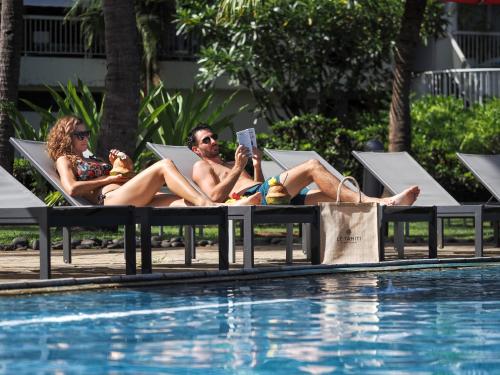 two people sitting in lounge chairs next to a swimming pool at Le Tahiti by Pearl Resorts in Papeete