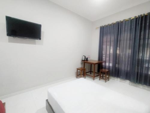 a room with a bed and a tv and a table at RedDoorz Syariah Near Stasiun Purwokerto in Purwokerto