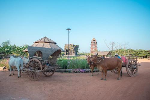 un par de vacas de pie junto a un carruaje tirado por caballos en อีสานบ้านเฮาฟาร์ม Esan Banhao Farm, en Ban Om Ko