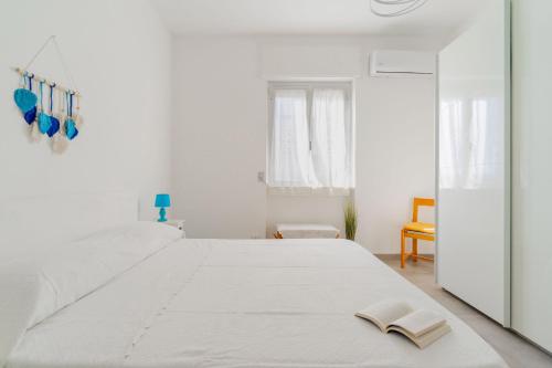 Un dormitorio blanco con una cama grande con un libro. en Terrazza vista mare e box auto en Gallipoli