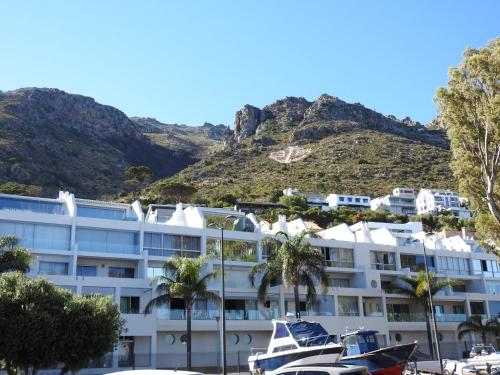 a hotel with palm trees and a mountain in the background at 24 Gordonia, Sleeps 7, Beach Front condo - Load-shedding friendly with Solar Power and battery backup in Gordonʼs Bay