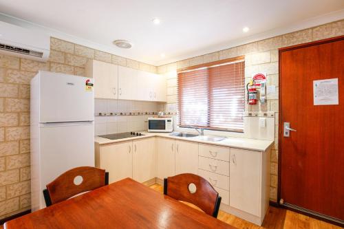 a kitchen with a table and a white refrigerator at Kalbarri Tudor Holiday Park in Kalbarri