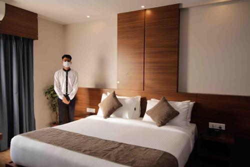a man wearing a mask in a hotel room with a bed at Hotel Tree Fern in Dibrugarh