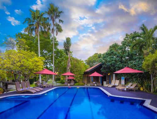 a pool at a resort with chairs and umbrellas at Chaarya Resort & Spa in Tissamaharama