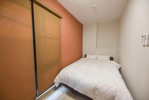 a small bedroom with a white bed and an orange wall at 4S STAY Awaikeda ikedaonsenyoko in Miyoshi