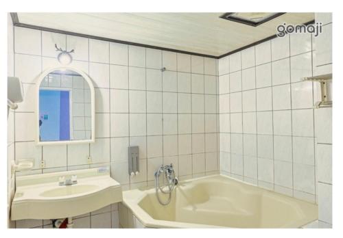 逸仙溫泉旅宿Yi-Shian Hotsprin House في Wenquan: حمام من البلاط الأبيض مع حوض استحمام ومغسلة