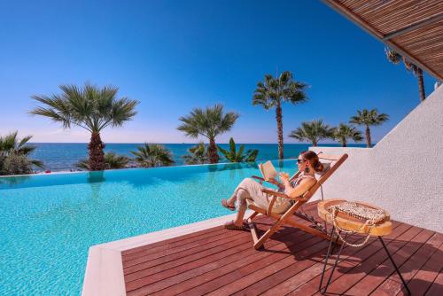 a woman sitting in a chair with a laptop next to a pool at Flora Garden BEACH - Couples Concept - Adults over 16 Only in Kızılot