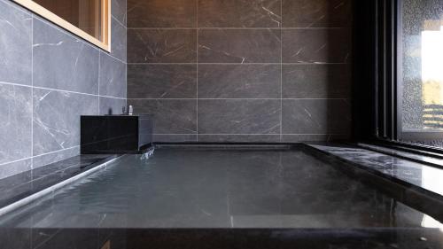 a bathroom with a swimming pool in a black tiled room at Sengokubara COCON in Hakone