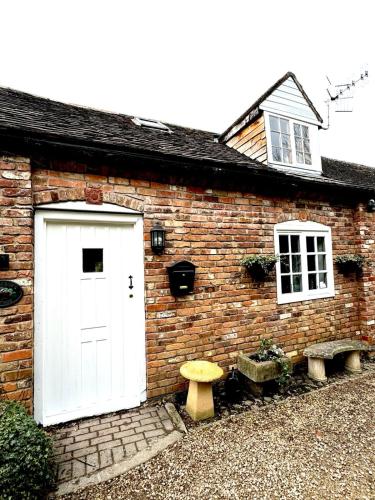 a brick house with a white door and two benches at Stable boys cottage in Sedgeberrow