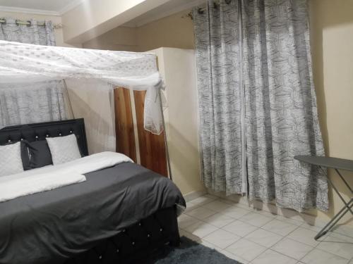 a bedroom with a bed and curtains and a desk at Jabali- Zuriel homes 1 bedroom apartment in Kakamega