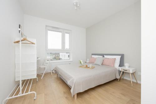 ein weißes Schlafzimmer mit einem Bett und einem Fenster in der Unterkunft Bright Pastel Apartment with Desk for Remote Work, Balcony and Parking by Renters in Danzig