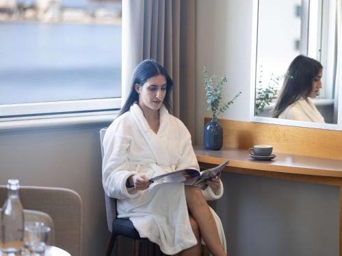 a woman sitting in a hotel room reading a book at Novotel Perth Langley in Perth