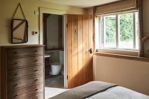 a bedroom with a dresser and a bathroom with a window at Stride’s Barn in Whiteparish