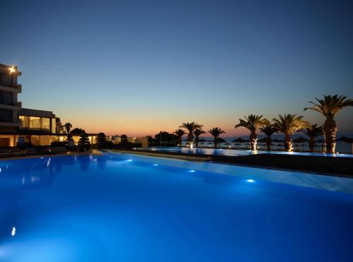 a large swimming pool with palm trees in the background at The Ixian Grand & All Suites - Adults Only Hotel in Ixia