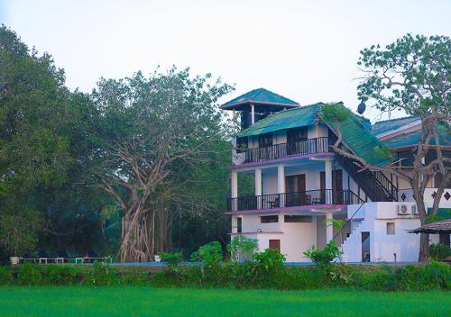 a white house with a green roof and trees at Birdsong Leisure Resort in Tissamaharama