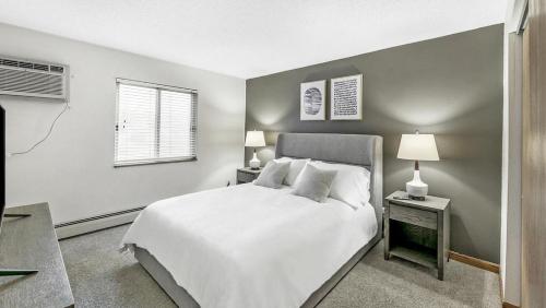 1 dormitorio con 1 cama blanca y 2 mesitas de noche con lámparas en Landing Modern Apartment with Amazing Amenities (ID1017X869), en White Bear Lake