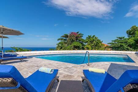 a swimming pool with blue chairs and an umbrella at Hospitality Expert Eden 7BR Pools Beach in Montego Bay