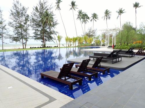 a pool with chairs and a table next to the water at RDHomeStay-RoxyBeachApt in Sematan