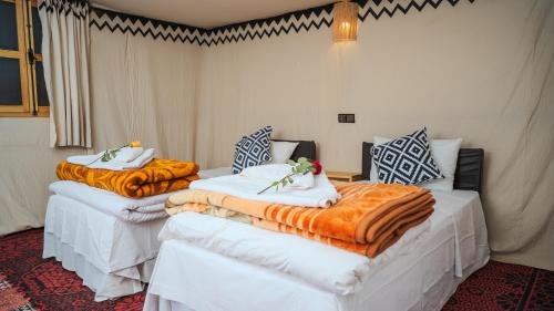 two beds in a room with orange and white blankets at Ame camp in Merzouga