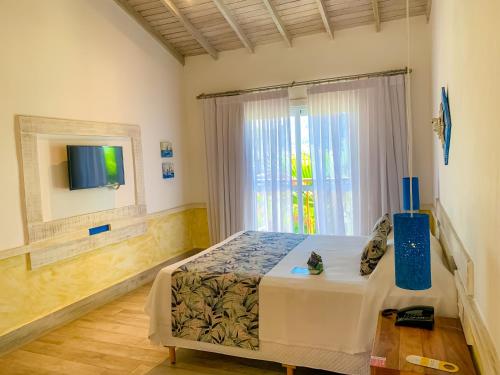 a bedroom with a bed and a tv and a window at Pousada Vila das Velas in Ilhabela