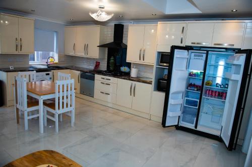 uma cozinha com armários brancos, uma mesa e um frigorífico em Newly Refurbished - Affordable Four Bedroom Semi-Detached House Near Luton Airport and Luton Hospital em Luton