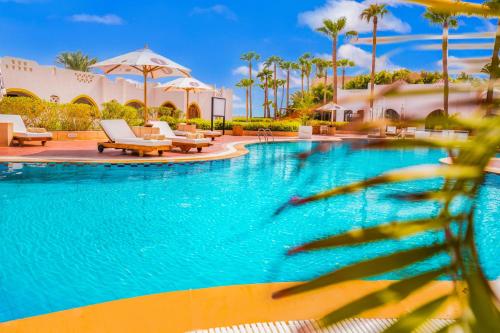 a large swimming pool with chairs and palm trees at Domina Coral Bay Resort, Diving , Spa & Casino in Sharm El Sheikh