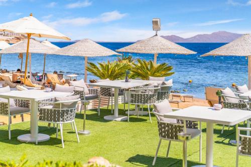 ein Restaurant am Strand mit Tischen und Sonnenschirmen in der Unterkunft Domina Coral Bay Resort, Diving , Spa & Casino in Sharm El Sheikh