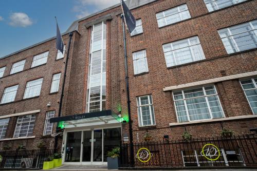 un bâtiment en briques avec des drapeaux verts devant lui dans l'établissement The Wesley Euston, à Londres