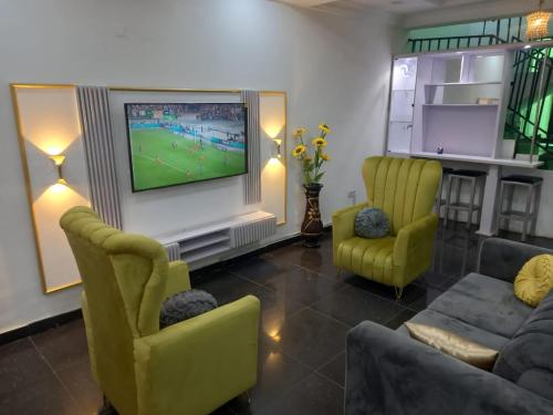 uma sala de estar com televisão e duas cadeiras amarelas em Mega Pavilion Apartment And Suits Gwarinpa em Gwarinpa